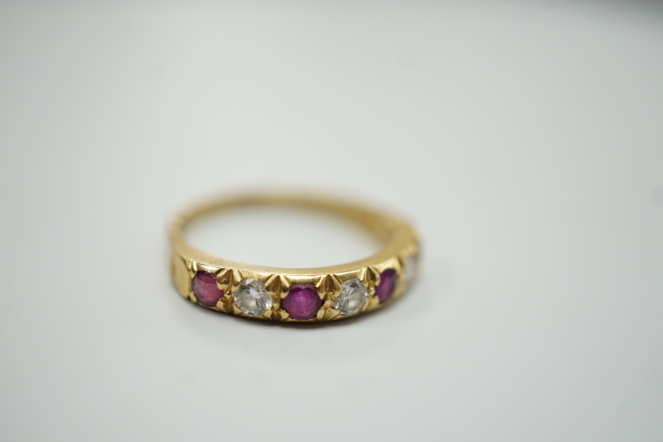 A modern 18ct gold, four stone ruby and three stone diamond set half hoop ring, size L/M